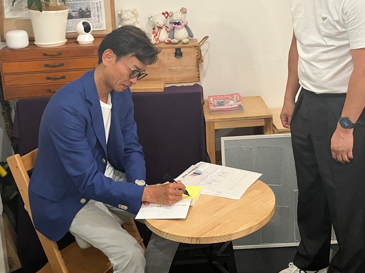 著書「コスパ悪いほうが人生は上手くいく」にサインをする山﨑幸治さん
